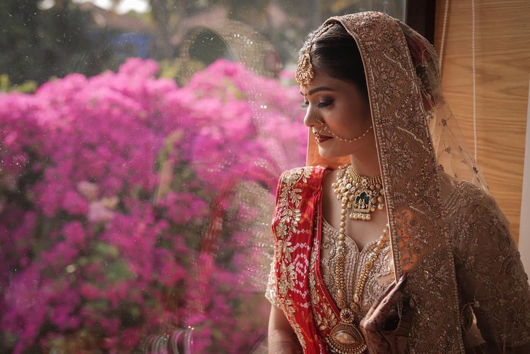 Bride standing in soft window light beside pink flowers